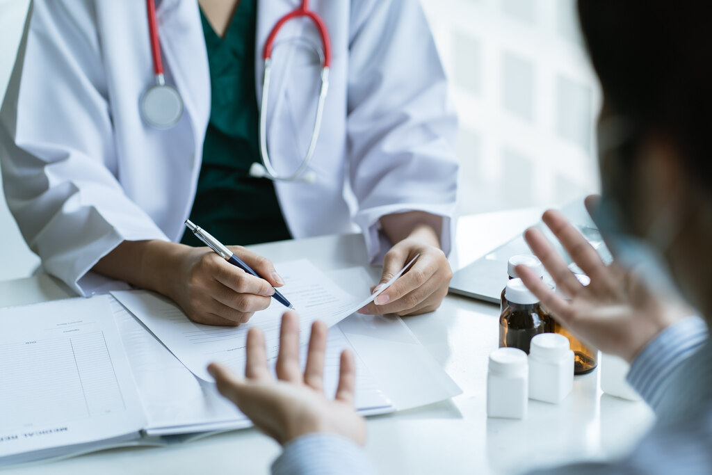 Profissional de saúde anota informações enquanto conversa com paciente e revisa prescrição médica.